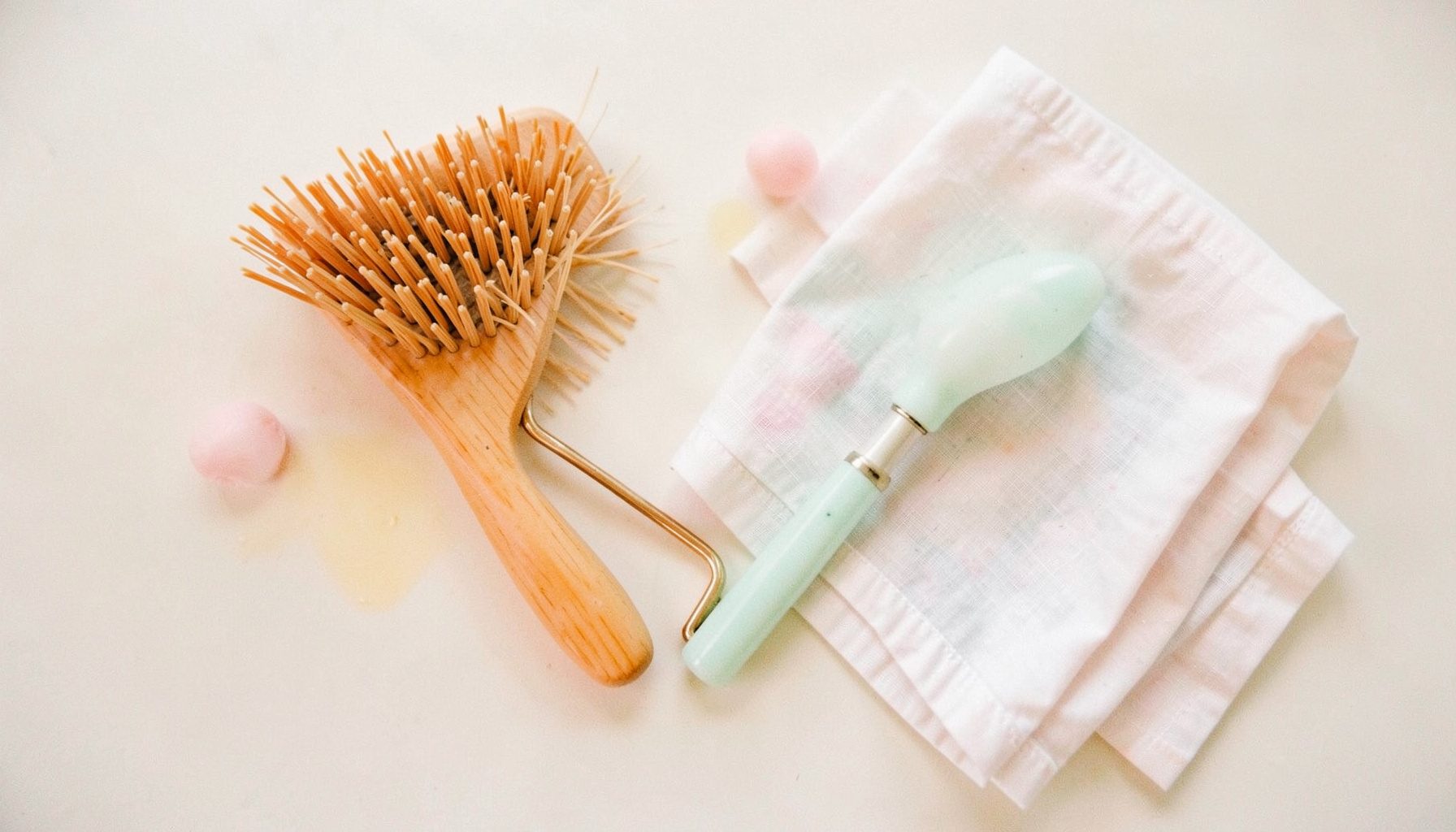 A flat lay of bamboo brushes, a jade roller, and a folded muslin cloth on a pale background, soft pastel accents